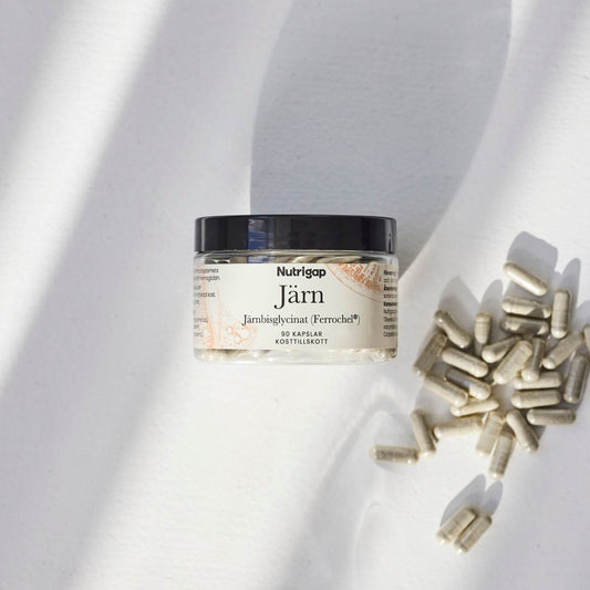 Burk med järntillskott i solljus med kapslar bredvid på vit bakgrund