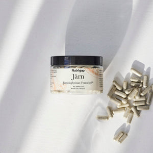 Burk med järntillskott i solljus med kapslar bredvid på vit bakgrund